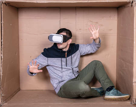 man with glasses for virtual reality, sitting in a cardboard room and entertainedの写真素材