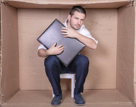 businessman with a briefcase sits in a tight cardboard box imitating an officeの写真素材