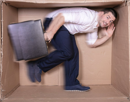 businessman with a briefcase sits in a tight cardboard box imitating an officeの写真素材