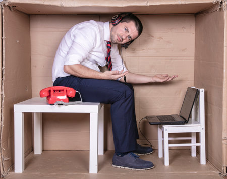 businessman in a cramped cardboard office trying to focus on his workの写真素材