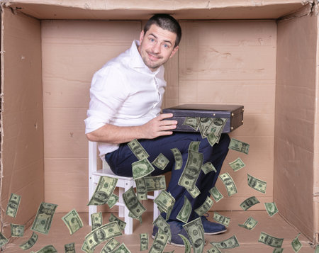 businessman with a briefcase sits in a tight cardboard box imitating an officeの写真素材