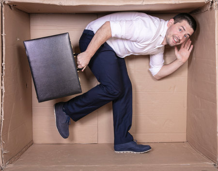 businessman with a briefcase sits in a tight cardboard box imitating an officeの写真素材