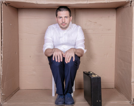 businessman with a briefcase sits in a tight cardboard box imitating an officeの写真素材