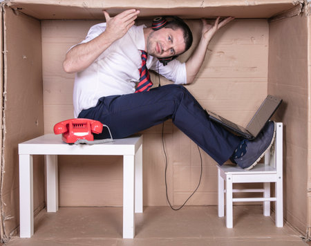 businessman in a cramped cardboard office trying to focus on his workの写真素材