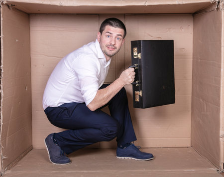 businessman with a briefcase sits in a tight cardboard box imitating an officeの写真素材