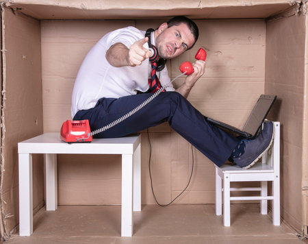 businessman in a cramped cardboard office trying to focus on his workの写真素材