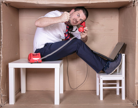 businessman in a cramped cardboard office trying to focus on his workの写真素材