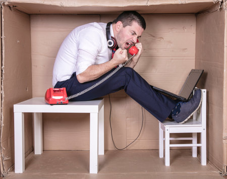 businessman in a cramped cardboard office trying to focus on his workの写真素材