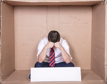 devastated unemployed businessman sitting in cardboard box, no job, copy spaceの写真素材