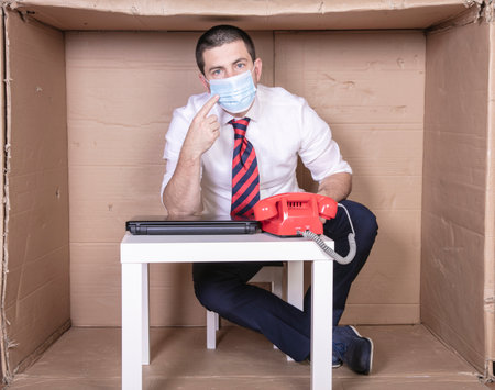 businessman pointing to a protective mask, sitting in his little cardboard officeの写真素材
