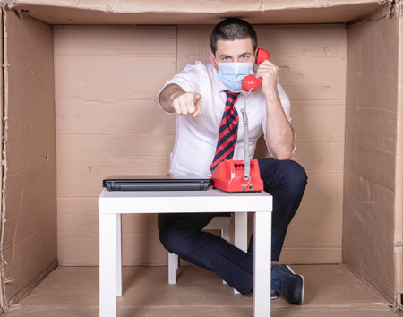 businessman with a protective mask on his mouth conducts a conversation on the phone, points his finger at youの写真素材