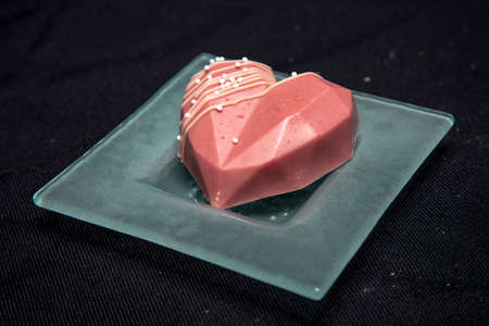 beautiful chocolate heart-shaped cupcake lies on a glass saucer, isolated on a black backgroundの写真素材