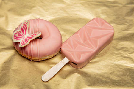 beautiful pink donut with butterfly and chocolate ice lie on golden backgroundの写真素材