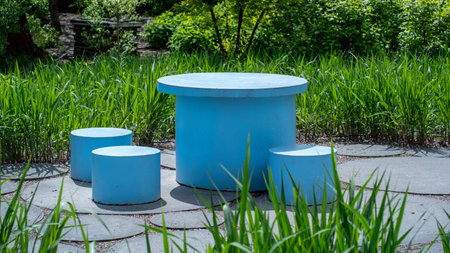 Three blue round stone benches in the garden with grass and bushes.の写真素材