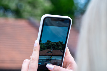 Woman taking a picture of a house with a smart phone in her handの写真素材