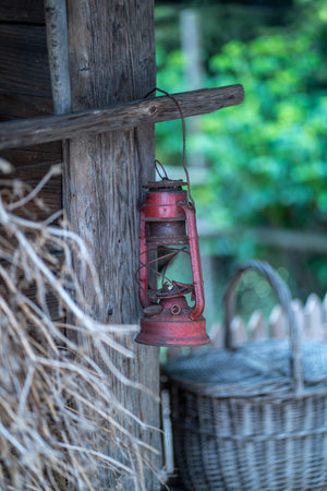 Old red lamp hanging on a wooden wall with basket in the backgroundの写真素材