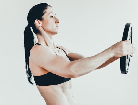 Sportive athletic woman lifting heavy barbells in light spacious