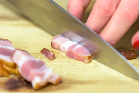 Hand holding knife and cutting bacon on the  wooden board - closeupの写真素材
