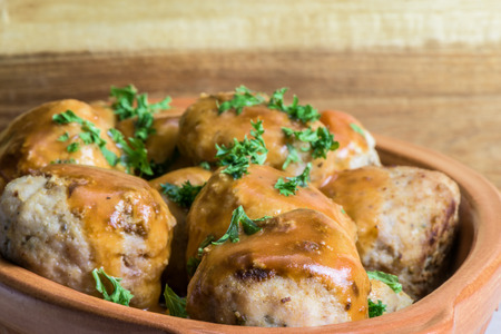 Fried meatballs in tomato sauce with parsley - wooden background - closeup.