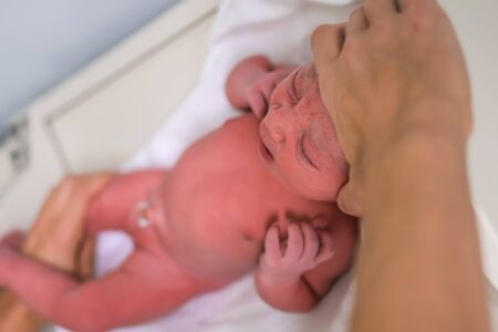 A newborn baby looking smart at the camera and is examinate in hospital just after childbirth....