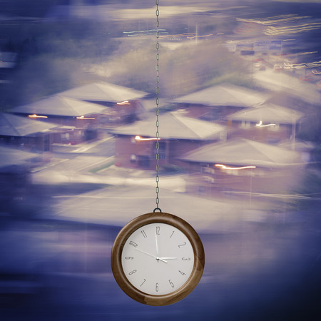 Time to Invest concept. Modern clock hanging on chain on blurred homes background.Time for home.の写真素材