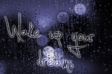 Sentence Wake up your dreams written on a wet glass. Night city life through windscreen: darkness...