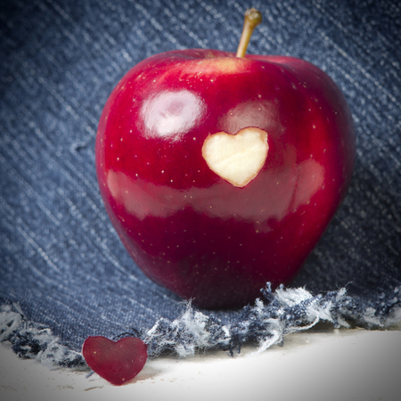 Fresh red apple with a heart shaped cut-out on jeans background. GMO free genetically modified organisms. Mothers day.の写真素材