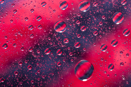 Close-up on water drops background on red and black surface. Water droplets with reflections in...
