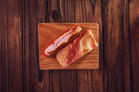 A piece of fresh bacon isolated on the wood background - Top viewの写真素材
