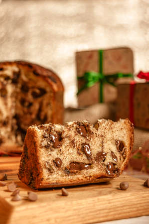 Slice of chocolate panettone on wooden cutting board with christmas ornaments