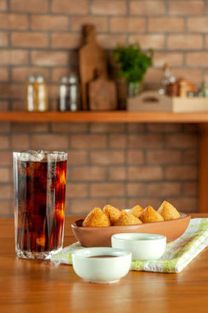 Fried Brazilian chicken croquettes with iced soda in a kitchen with bricks wall.の写真素材