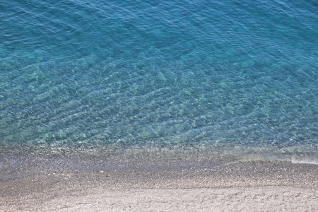 Blue sea water surface with sand and pebble beach in Greeceの写真素材