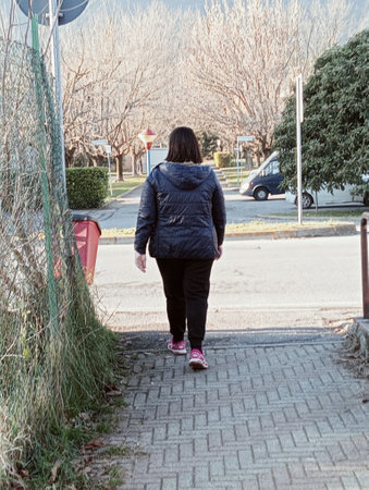 Back view of a woman walking along a paved street in winter.の写真素材