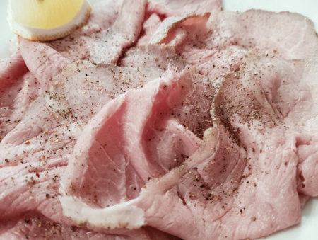 Slices of ham with lemon and spices on white plateの写真素材