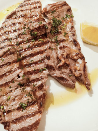 grilled beef steak with lemon and parsley on a white plateの写真素材