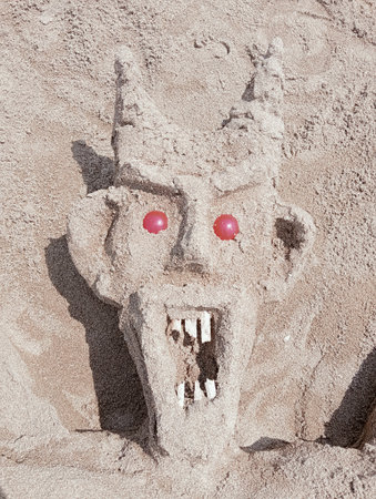 Sand castle on the beach in the form of a monster with red eyes