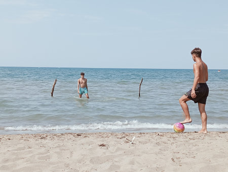Two boys playing on the beach with a ball and a stick.の写真素材