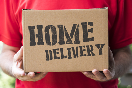 Delivery at home concept: a shipping box brought by hand with "home delivery" textの写真素材