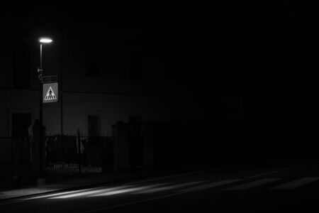 Monochrome shot of a street lamp, which illuminates the pedestrian crossing at night, imprinted on the roadway, for pedestrian safetyの写真素材