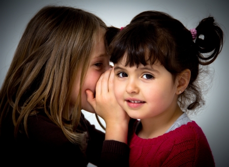 portrait of two little girls telling secretsの写真素材