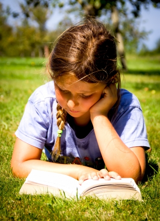 little girl reading a book in a meadowの写真素材