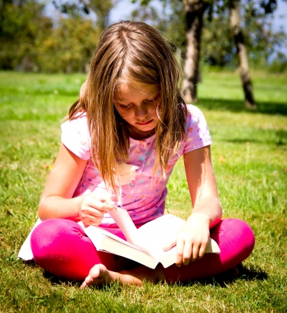 little girl reading a book in a meadowの写真素材