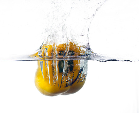 yellow pepper falling and splashing into clear water.の写真素材