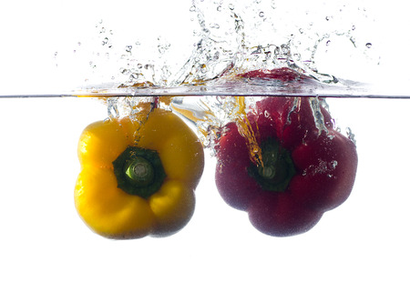 red and yellow pepper falling and splashing into clear water.の写真素材