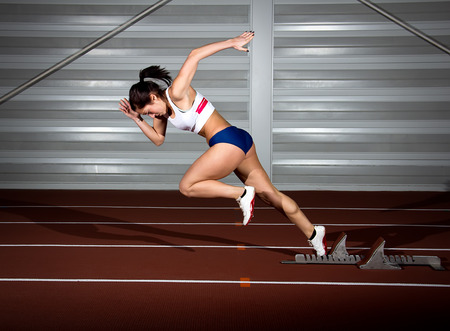 Woman sprinter leaps from starting block.の写真素材