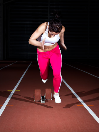 Woman sprinter leaps from starting block.の写真素材