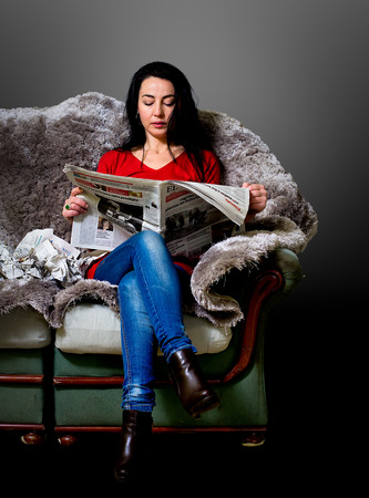 Woman reading the newspaper and sitting on a sofaの写真素材