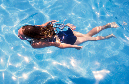 Beautiful little girl diving in pool with pink gogglesの写真素材