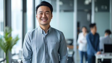 Portrait of a handsome smiling asian businessman boss standing in his modern business company office.の素材