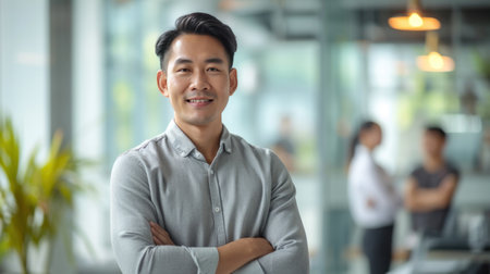 Portrait of a handsome smiling asian businessman boss standing in his modern business company office.の素材